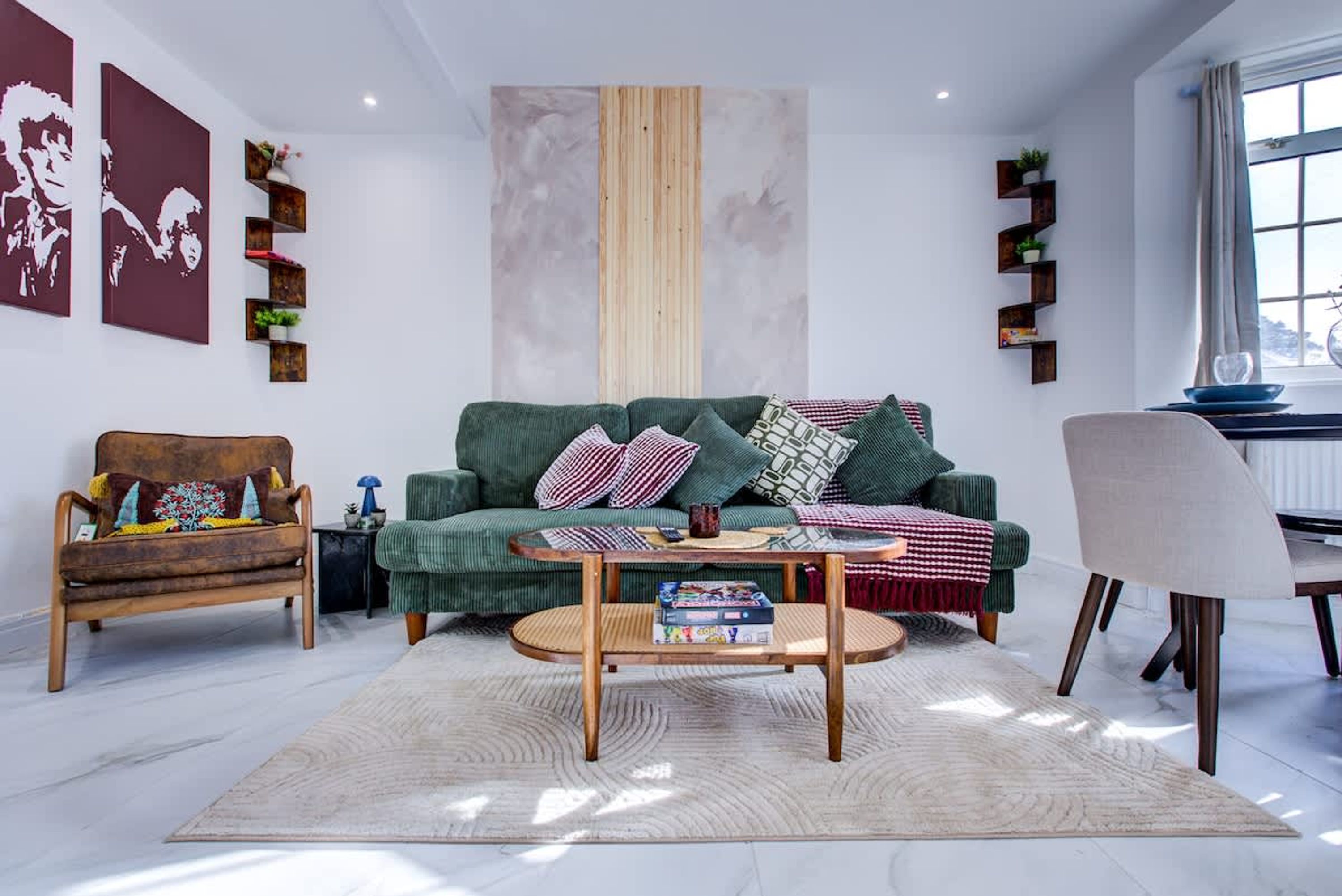 Ein Wohnzimmer mit einem grünen Sofa, einem Holztisch und einem Sessel. An den Wänden befinden sich Regale mit Pflanzen und Kunstwerken.