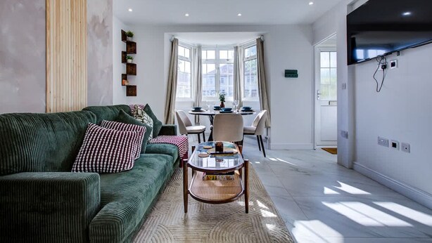 En moderne stue med en grøn sofa, et glasbord og et spiseområde med bord og stole.