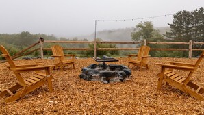 Un área de estar al aire libre rústica con sillas Adirondack, un pozo de fuego y una valla de madera.