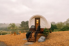 A covered tent with a wooden door and a staircase leading up to it, surrounded by a wooden fence and trees.