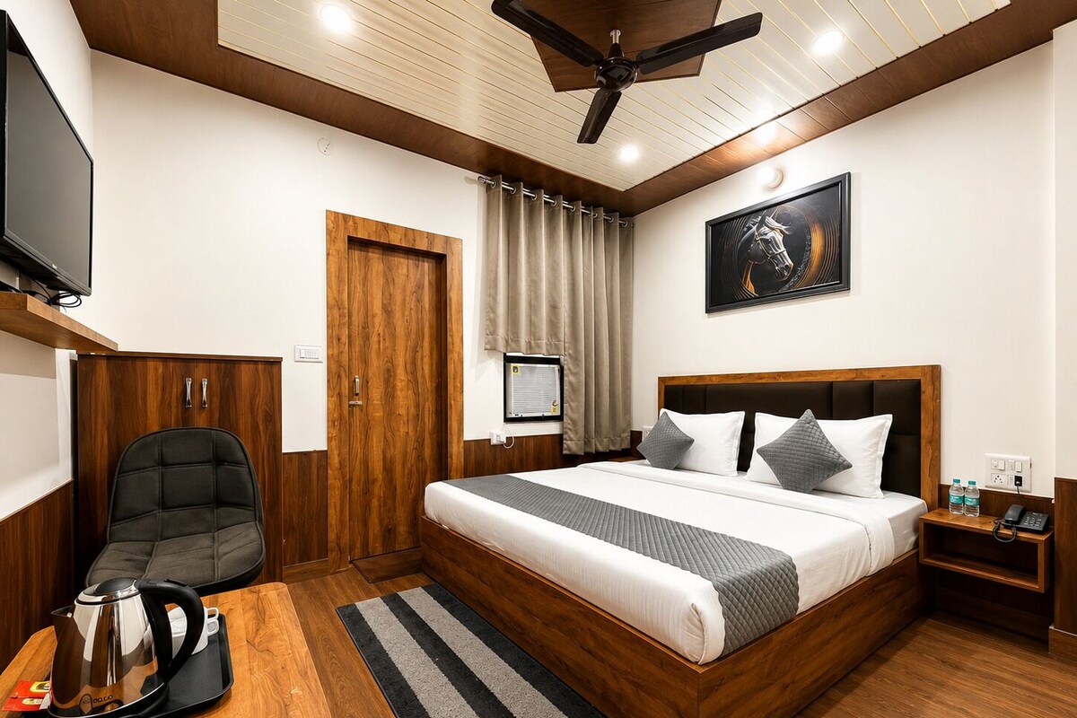 Een hotelkamer met een bed, een bureau met een waterkoker, een stoel, een plafondventilator en een schilderij aan de muur.