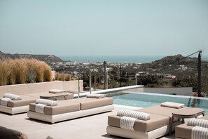 Ein Rooftop-Endlospool mit beigen Liegestühlen und Blick auf die Stadt.