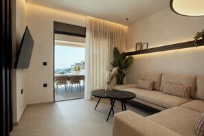 Ein modernes Wohnzimmer mit einer Couch, einem Couchtisch, einem an der Wand montierten Fernseher und Blick ins Freie durch ein großes Fenster.
