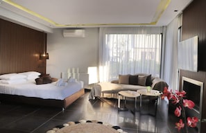 A modern hotel room with a bed, sofa, coffee table, and a fireplace. - Heaven Horizon Villa - Ethereal and Blissful Gem (Pangaio)