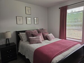 A bedroom with a bed, a nightstand, a lamp, and a window with blinds. - 2-bedroom townhome in St. Augustine (St. Augustine)