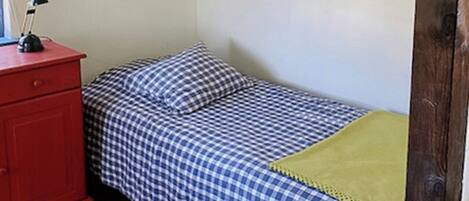 Une petite chambre à coucher avec un lit, une commode rouge, une bibliothèque et un tableau encadré au mur.
