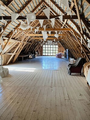 An attic room with a sloped wooden ceiling, a large window, and a wooden floor. - Farm on Gotland with fruit trees near harbour (Slite)