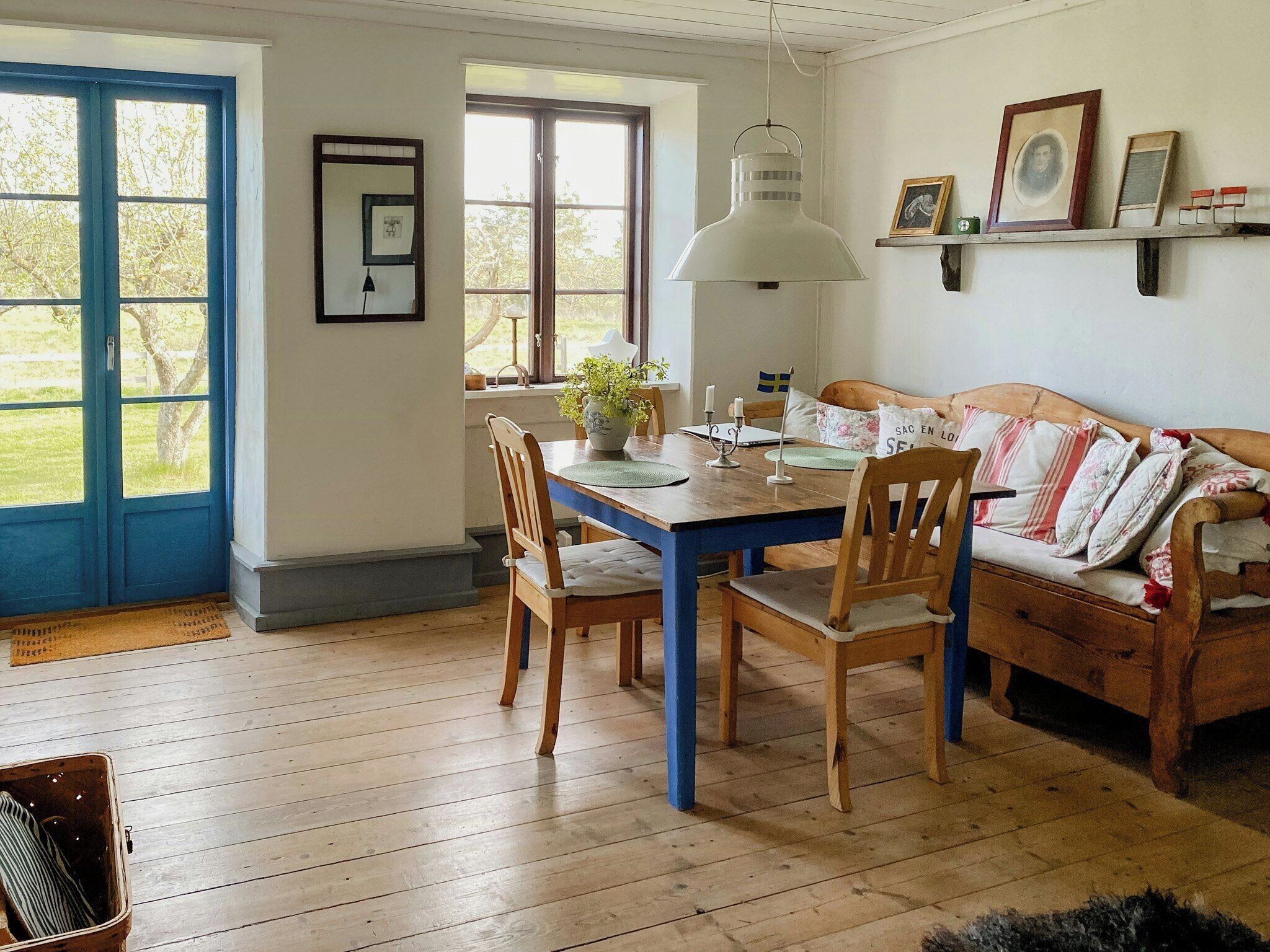 A dining area with a wooden table, chairs, a hanging light fixture, and a sofa with cushions.