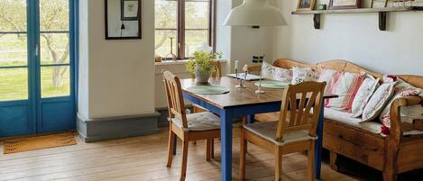 A dining area with a wooden table, chairs, a hanging light fixture, and a sofa with cushions.
