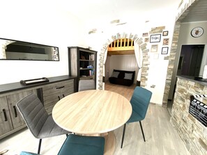Ein modernes Interieur mit einem runden Holztisch, zwei blauen Stühlen, einem Fernseher, einem Bücherregal und einer gemütlichen Sitzecke mit einer Couch und einem Durchgang.