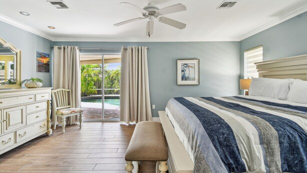 A bedroom with a bed, a bench, a dresser, a chair, a ceiling fan, and a view of the outdoors. - Sunnyside Up Cottage - Walk to Siesta Beach, Waterfront Home by The Bay & Key Collection (Siesta Key)