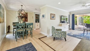 A spacious living room with a dining area, a kitchen, and a balcony with a view. - Sunnyside Up Cottage - Walk to Siesta Beach, Waterfront Home by The Bay & Key Collection (Siesta Key)