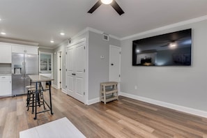 A modern kitchen with white cabinetry, a stainless steel refrigerator, and a bar area with stools.