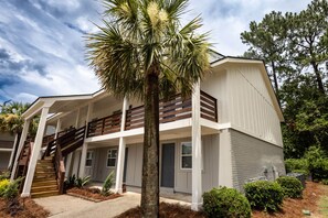 A two-story building with a covered porch, a staircase, and a palm tree in the foreground.