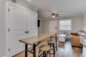 A kitchen with a wooden table, bar stools, a ceiling fan, and a window with blinds. - Pines at 5 Corporate Furnished Rentals Suite 214 (Hephzibah)