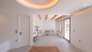 A spacious room with a curved sofa, a small side table, and a large window. - The Lofts Paros Executive Suites (Naousa)
