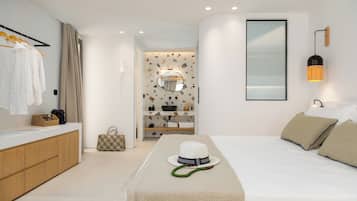 Un dormitorio moderno con una cama grande, una mesita de noche, un espejo, un armario y un baño visible a través de una puerta abierta.