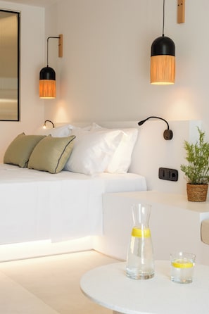 Une chambre à coucher moderne avec un lit, des lampes de chevet, une plante en pot et une table ronde sur laquelle se trouvent une carafe en verre et un verre.