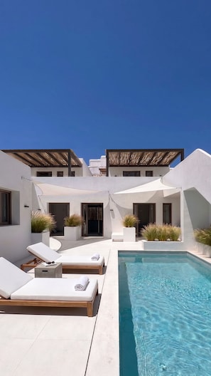 A modern outdoor pool area with lounge chairs and a clear blue sky. - The Lofts Paros Executive Suites (Naousa)