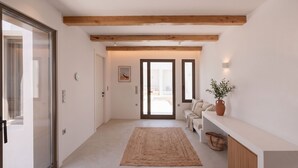 Un pasillo con techo de madera, una alfombra, un sofá, un jarrón con plantas y una puerta que da a otra habitación.