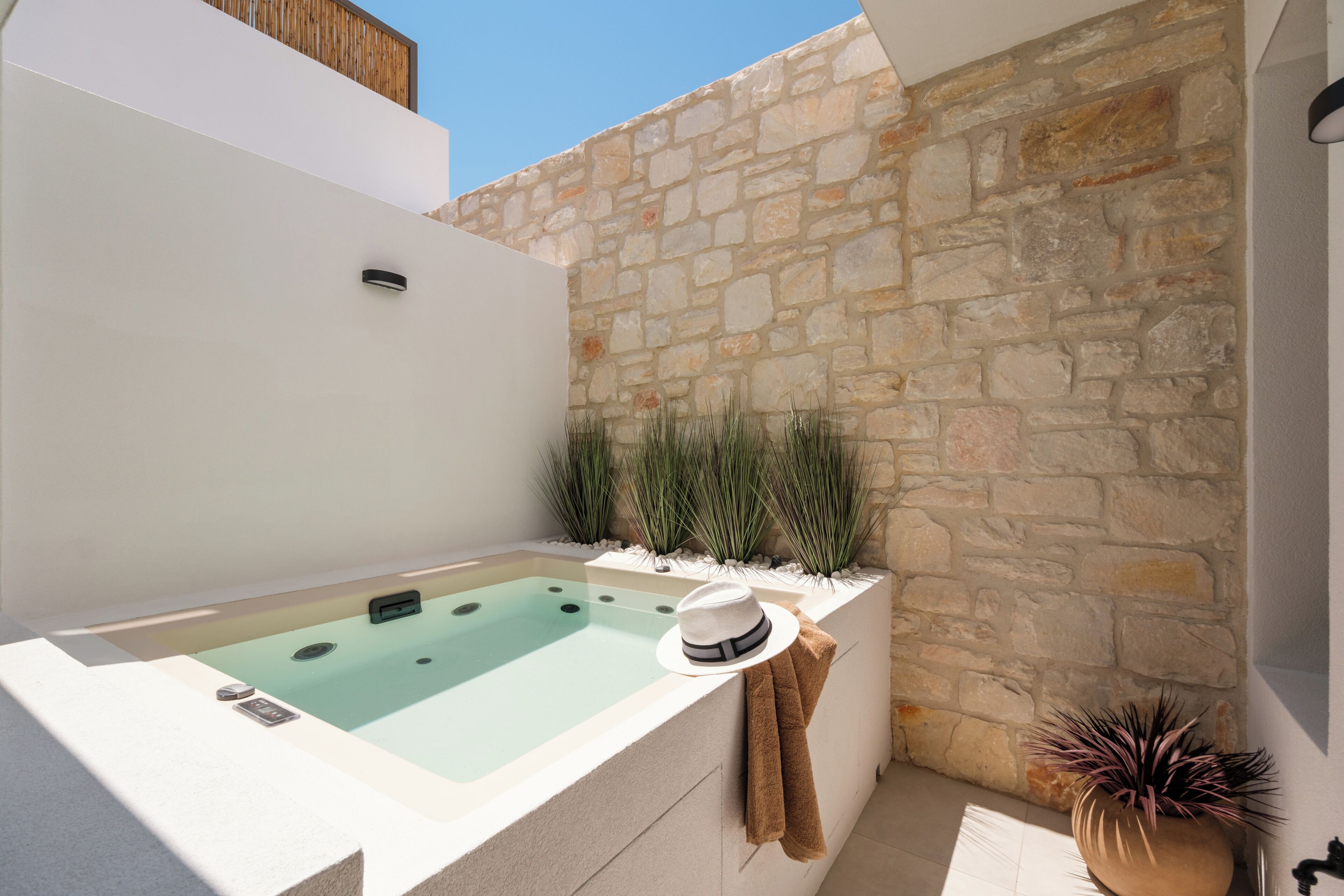 A spa area with a stone wall, a hot tub, and decorative plants.