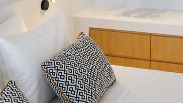 Quarto moderno com cama, travesseiros, luminária pendente, mesa de cabeceira e um cabideiro.