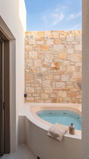 A spa area with a stone wall, a bathtub, and a towel. - The Lofts Paros Executive Suites (Naousa)