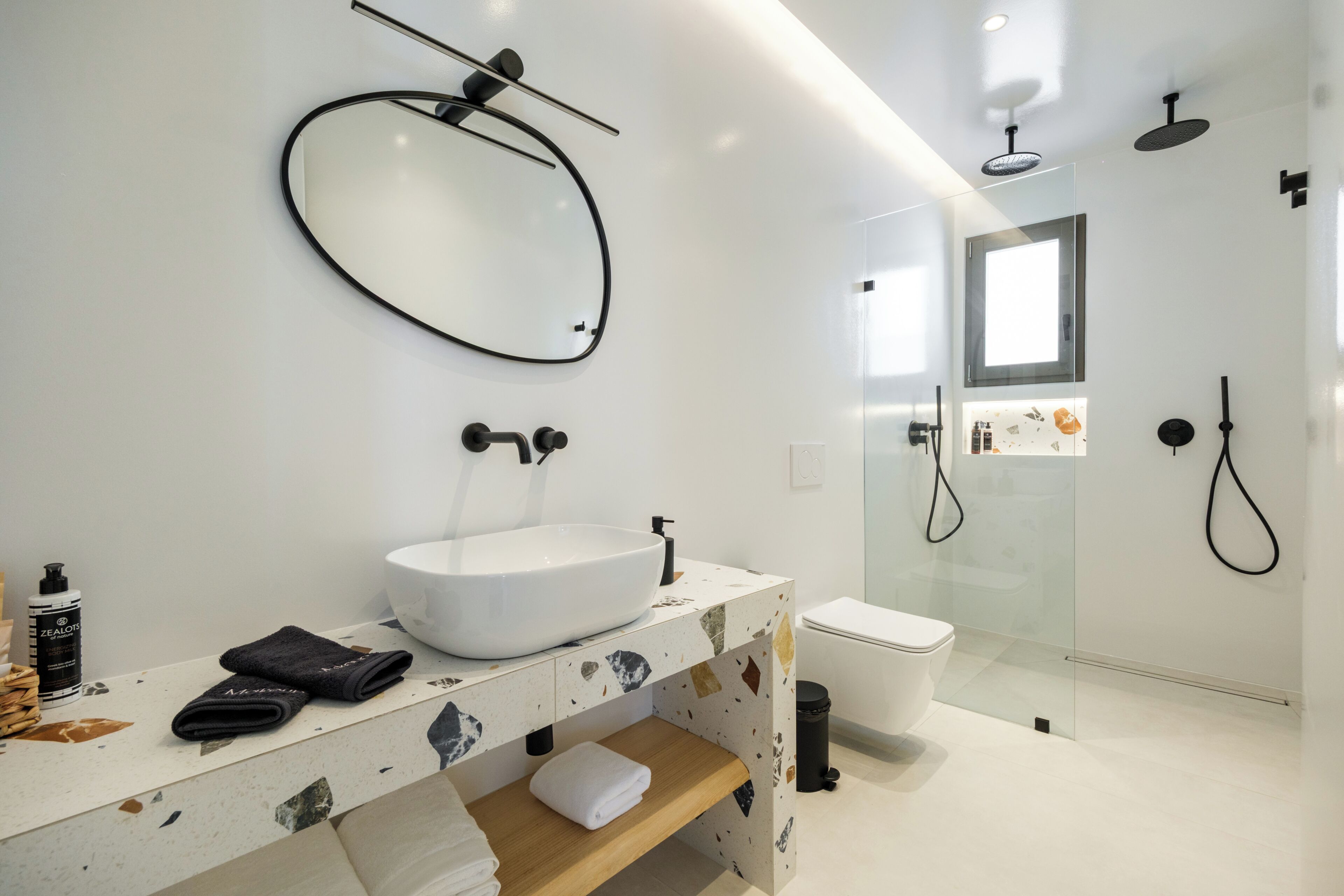 A modern bathroom with a large oval mirror, a vessel sink, a glass-enclosed shower, and a toilet.