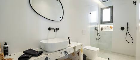 A modern bathroom with a large oval mirror, a vessel sink, a glass-enclosed shower, and a toilet.