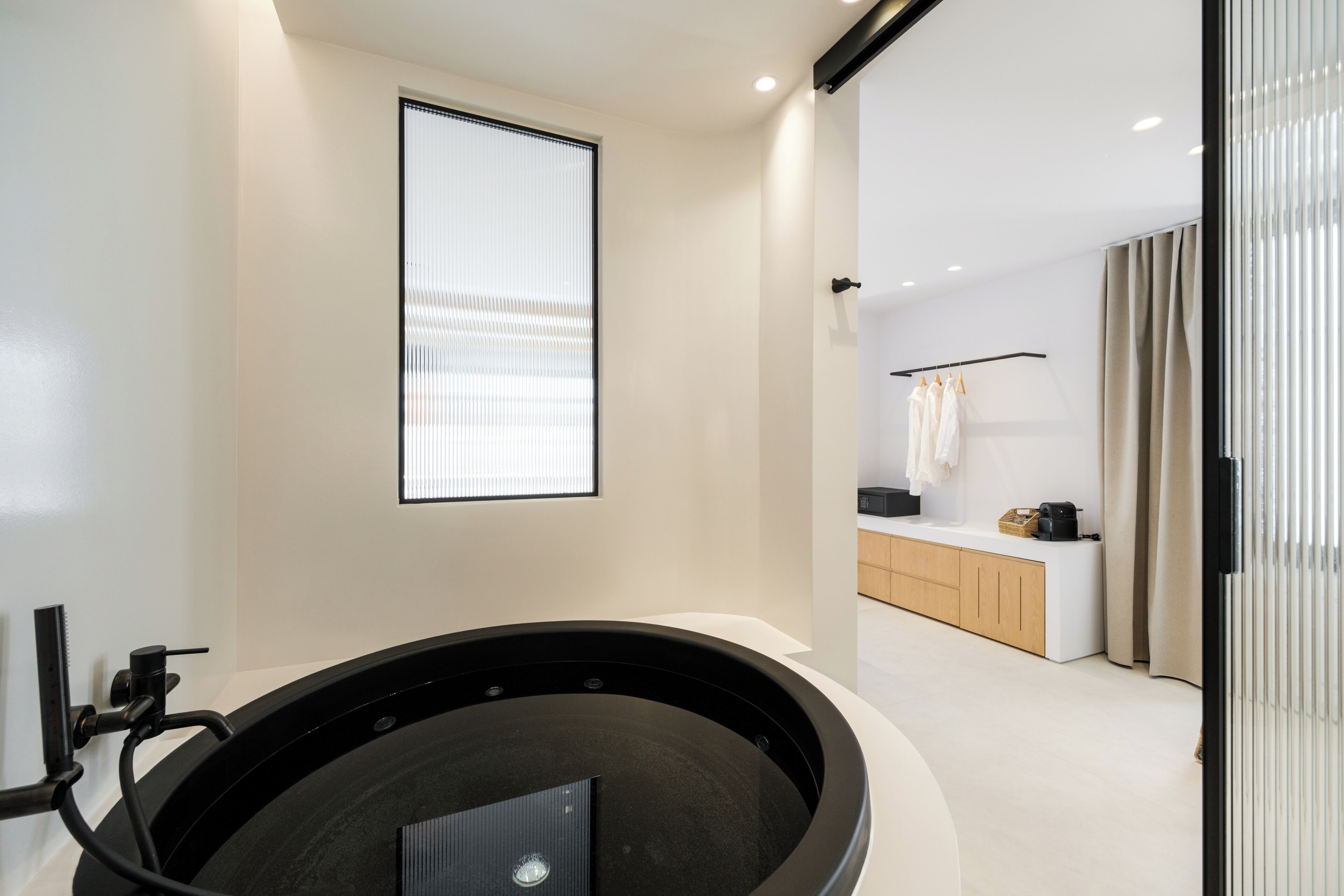 Uma casa de banho moderna com uma banheira preta, uma sanita e uma janela com persianas.