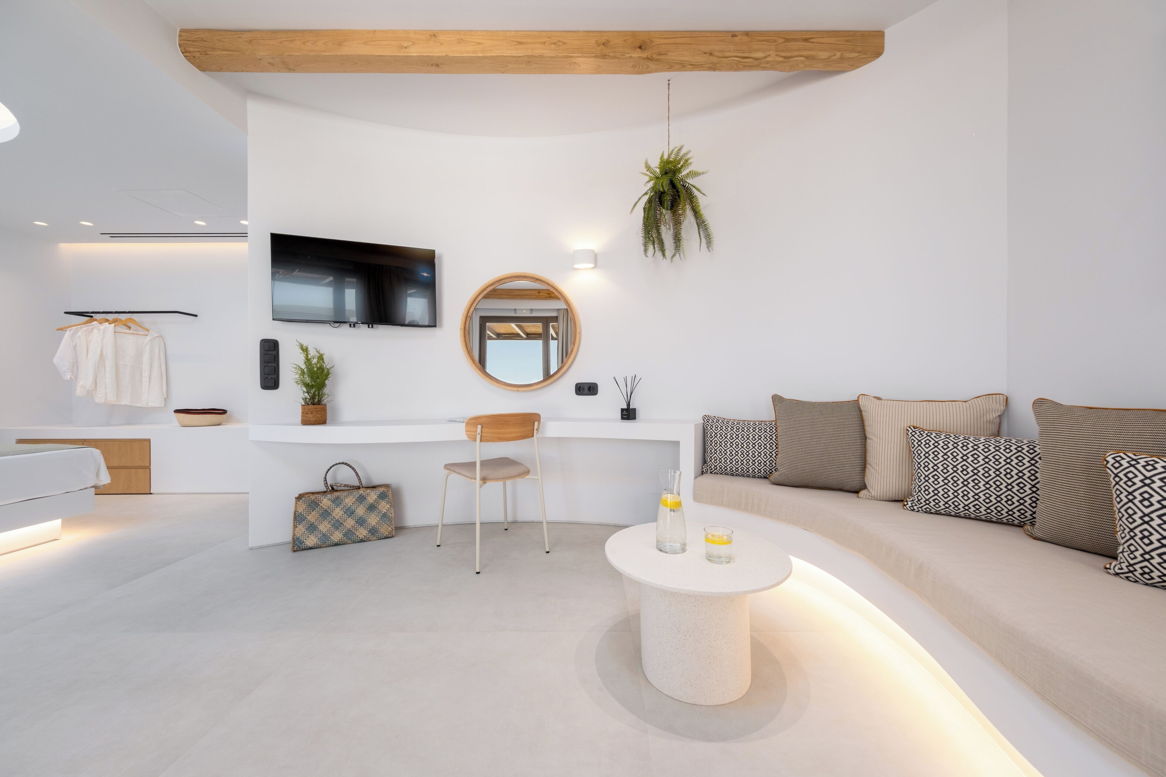 A modern living room with a flat-screen TV, a round mirror, a sofa with patterned cushions, and a coffee table with a vase and glasses.