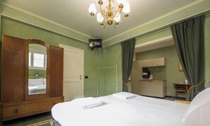 Habitación de hotel con cama, espejo, armario, kitchenette y candelabro.