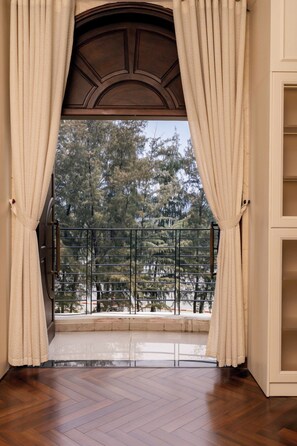 Une pièce avec un plancher en bois, un balcon doté d’une rambarde en métal et des rideaux de couleur beige.