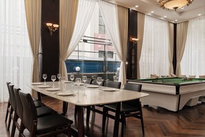 Un comedor con mesa de billar, mesa de comedor para seis personas y vistas a edificios a través de amplios ventanales.