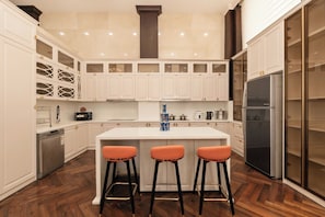 A modern kitchen with white cabinetry, a central island with stools, a dishwasher, and a refrigerator. - Mia Riverside Villa D7 with 9 bedrooms (Ho Chi Minh City)
