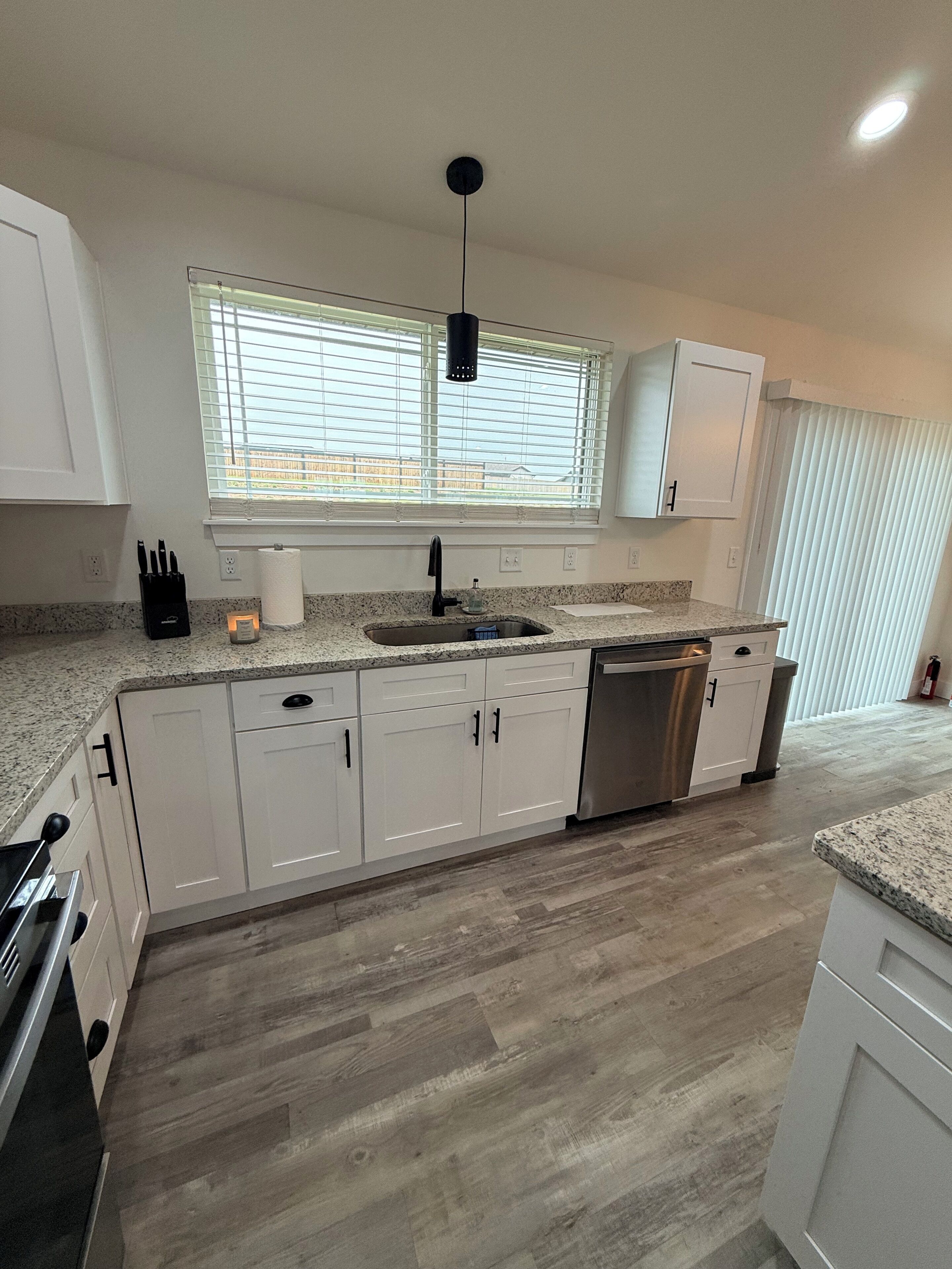 A modern kitchen with white cabinets, a stainless steel dishwasher, and a granite countertop.