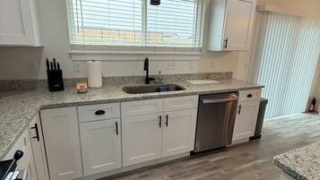 A modern kitchen with white cabinets, a stainless steel dishwasher, and a granite countertop.