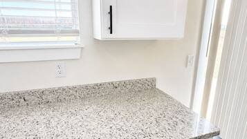 A kitchen with white cabinets, a granite countertop, a dishwasher, and a trash can.