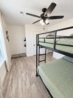 Een kamer met een stapelbed, een plafondventilator, een deur en een raam met gordijnen.