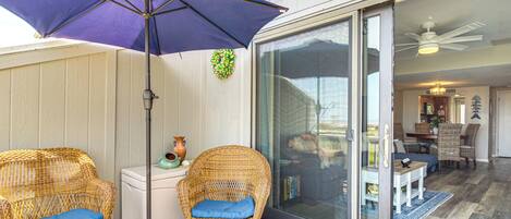 Een terras met rieten stoelen, een paarse parasol en een glazen deur die leidt naar een eethoek binnen.