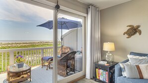 En balkon med fletmøbler, en potteplante og udsigt over havet.
