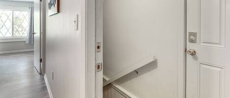 A hallway with a white door, a staircase, and a window with a view.
