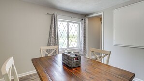 Una mesa de comedor de madera con sillas, una ventana con cortinas y vistas al exterior con vegetación.