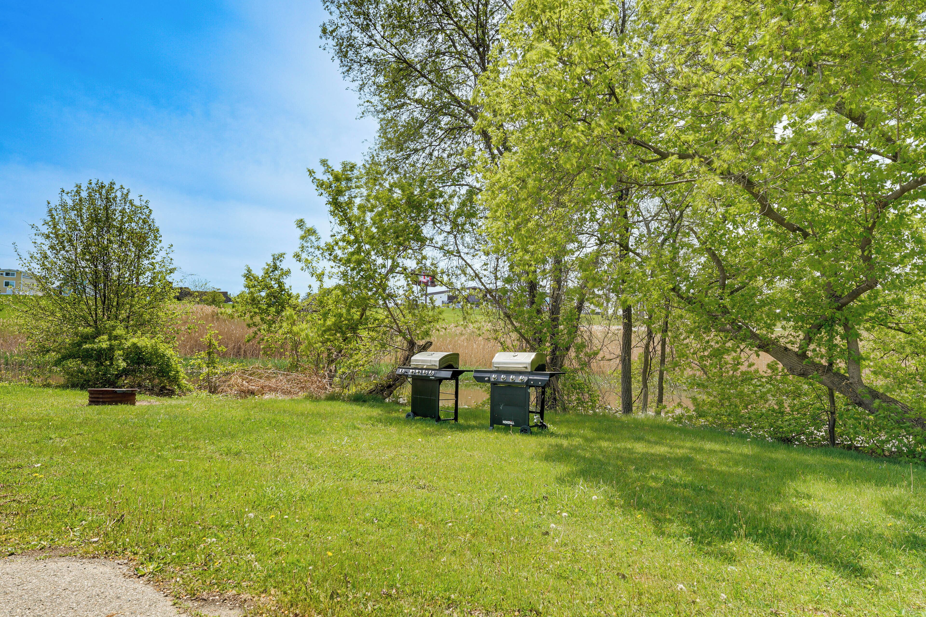 A grassy area with two barbecue grills and a bench.
