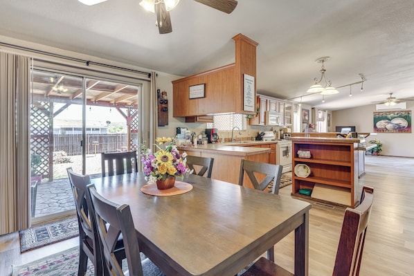 A kitchen with wooden cabinets, a dining table with chairs, a flower vase, and a clock on a shelf.