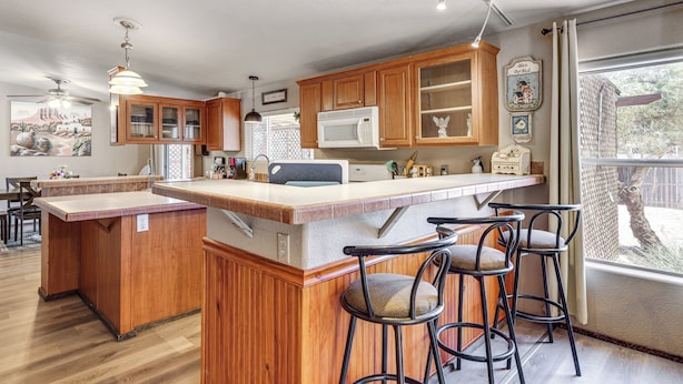 A kitchen with wooden cabinets, a microwave, and a bar area with stools. - 7 Miles to Roosevelt Lake! Mtn-view Family Escape (Tonto Basin)
