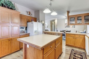 A kitchen with wooden cabinets, a refrigerator, a microwave, and a large island.