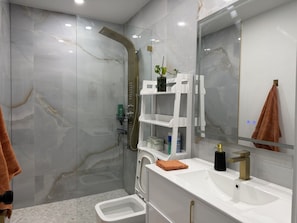 A modern bathroom with a glass-enclosed shower, a white vanity with a gold faucet, and a large mirror.