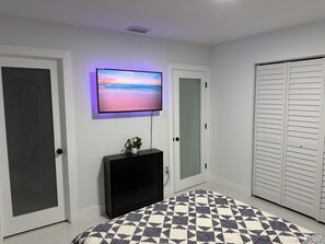 A bedroom with a bed, a TV on the wall, a dresser, a closet, and a patterned rug.