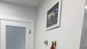 Une salle de bain avec une porte blanche, un porte-serviettes sur lequel est posée une serviette marron, et un tableau encadré accroché au mur.